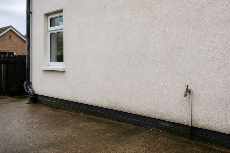 Plain rendered house wall beside a driveway with no EV charge point installed.