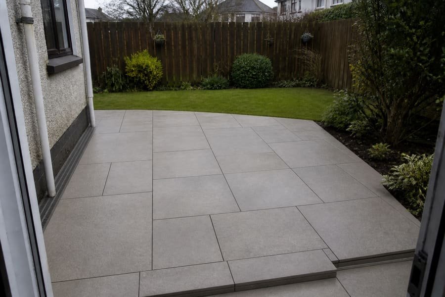 The same garden with a laid porcelain patio, reseeded lawn and planted borders.