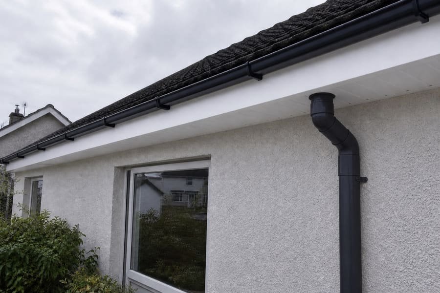 The same eaves with new white uPVC fascia and soffit, and a black gutter and matching black downpipe on even brackets.