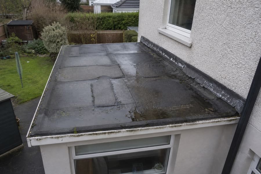 Worn flat roof with patched felt, ponding water and lifted seams.